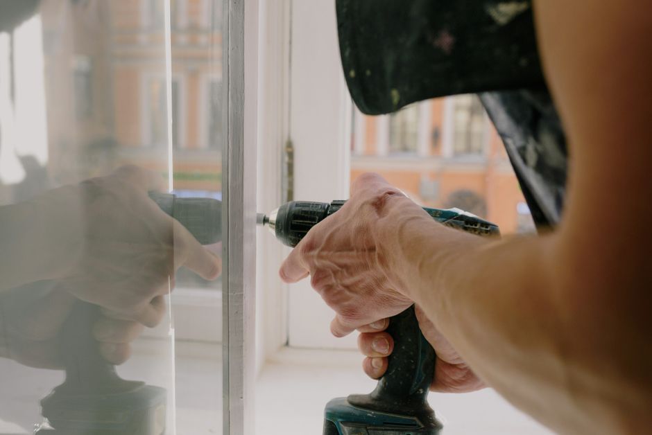A worker fitting a white window frame with a cordless drill.