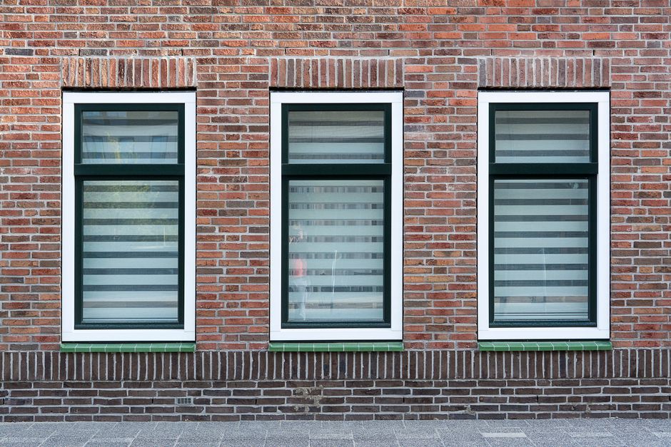A modern brick wall with three symmetrical windows featuring black and white striped blinds.